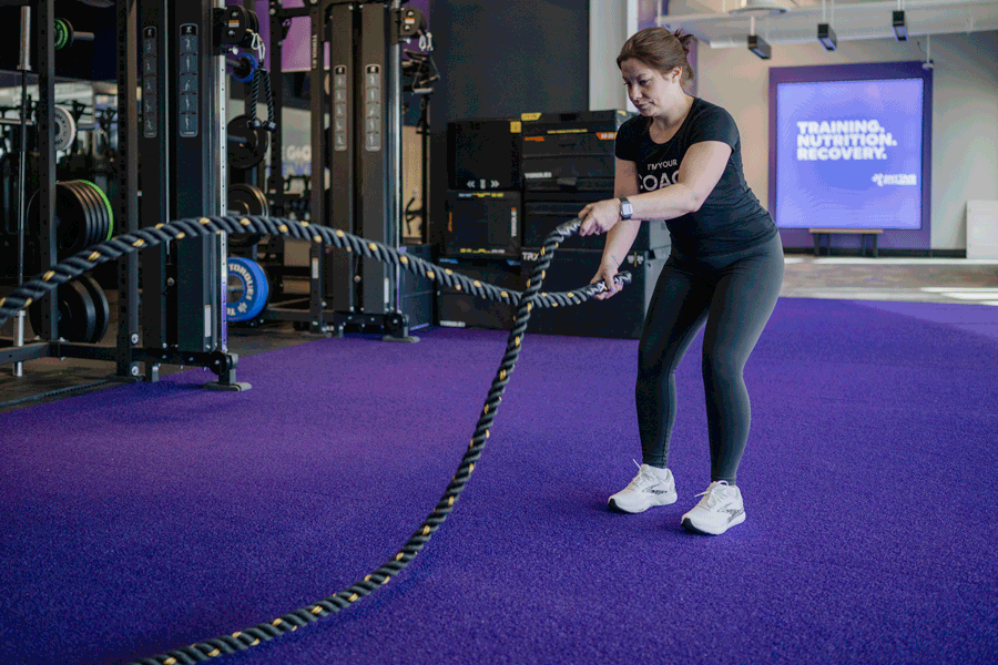 An Anytime Fitness Coach performing a speed wave with the battle ropes, targeting the upper back and core.