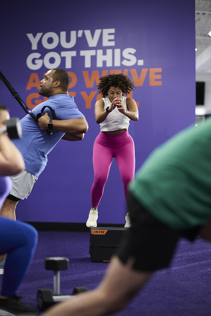 People in an Anytime Fitness gym participating in a group workout with a mix of cardio and strength exercises.