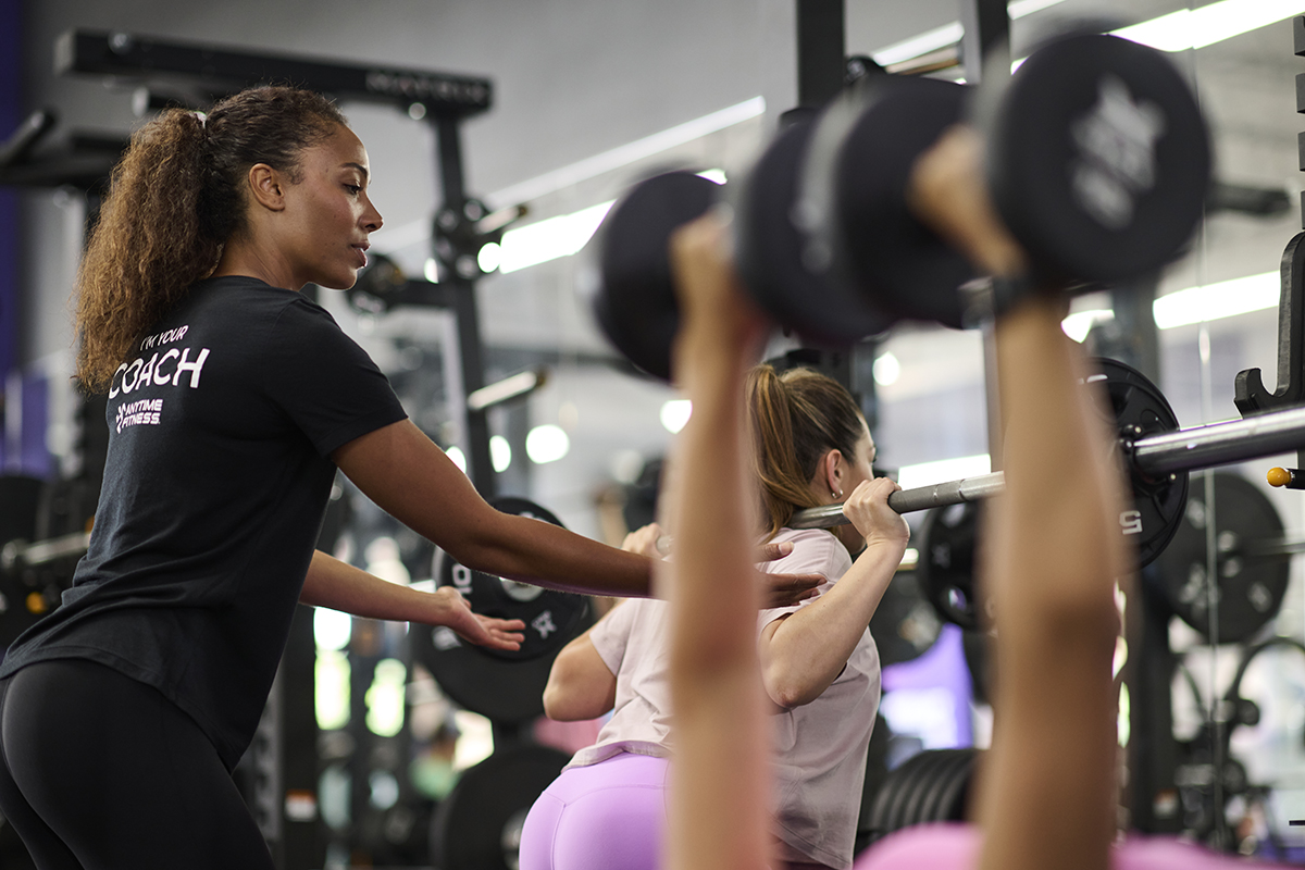 Anytime Fitness Coach spotting a gym member doing a back squat with a barbell.