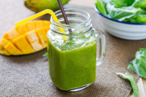 Glass with a green smoothie and straw, a cubed mango off to the side.