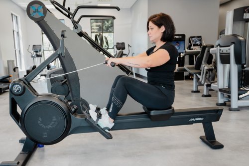 AnytimeFitness_RowingMachine_Step4 Coach Heather demonstrating the recovery step on a rowing machine.