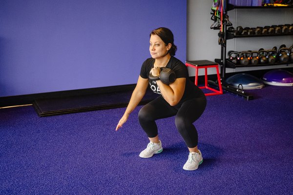 Coach squatting while doing a kettlebell workout in the gym.