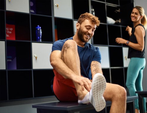 Man putting on shoes in the lobby of a gym with a workout buddy nearby.